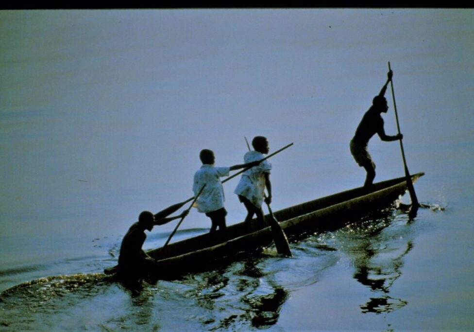 Unlike rowers, boys stand to row their pirogue on the Zaire River.